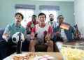 multiracial curious male friends with beer bottles flags ball watching soccer match home scaled